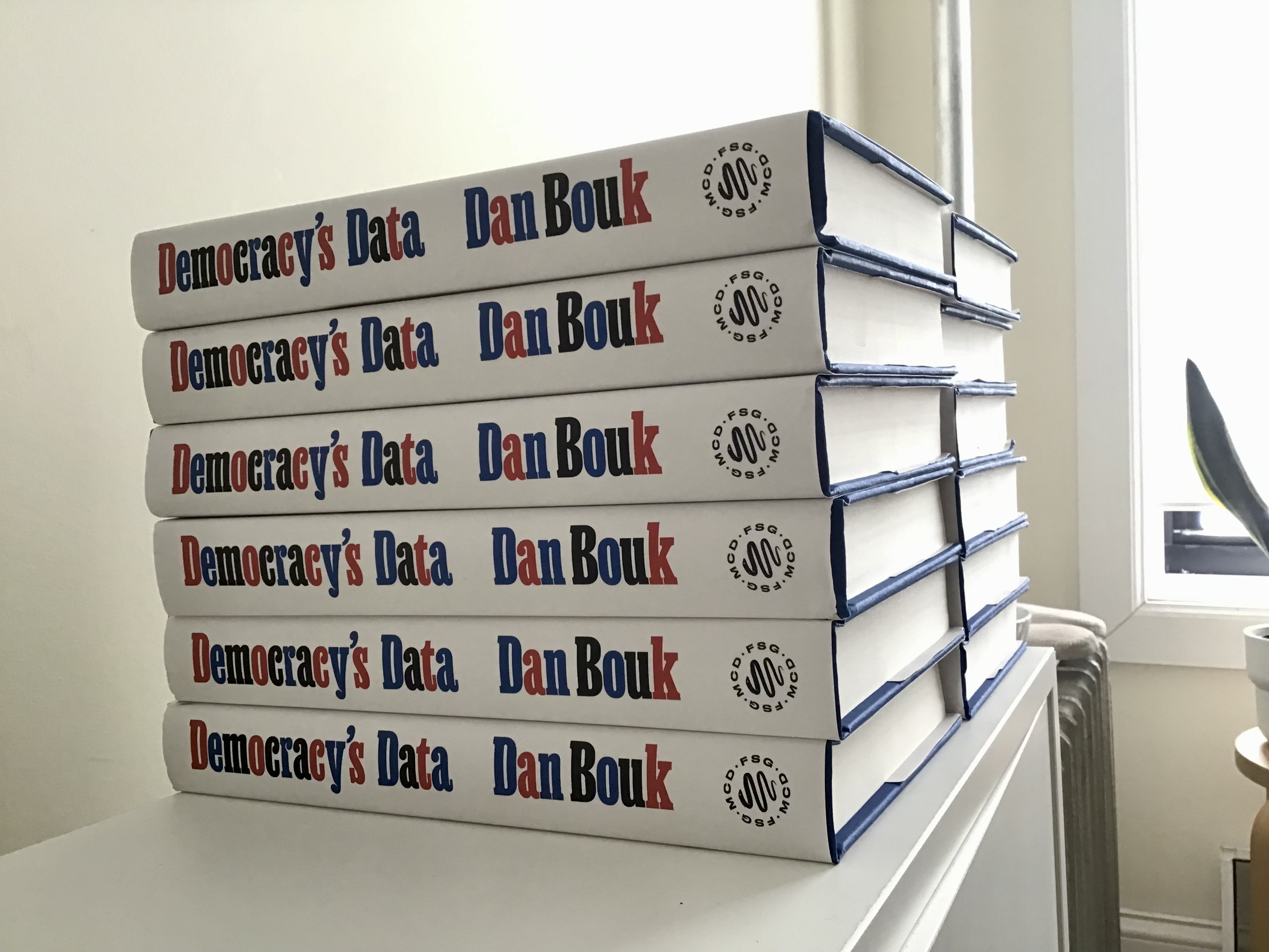 A stack of books lay on their sides, each bearing the title Democracy's Data by Dan Bouk.